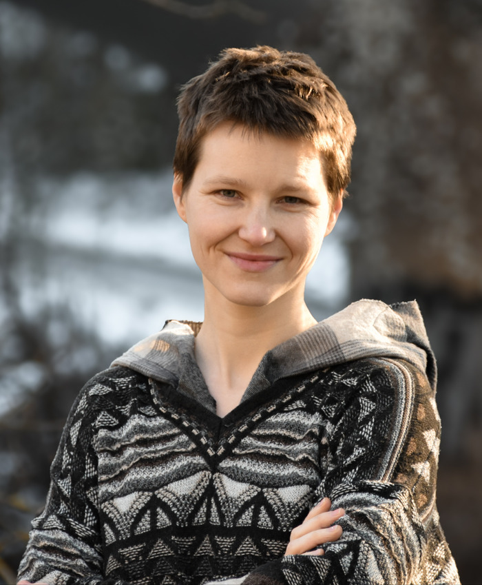 Mgr. Lori Lang Portrétová fotka Lori ve svetru na rozmazaném pozadí zimního lesa.